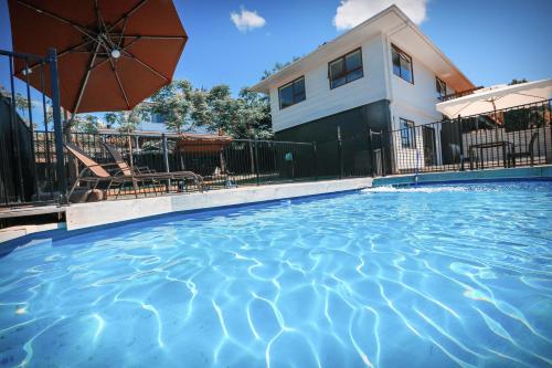 a swimming pool in front of a house with an umbrella at Swimming Pool Holiday Villa in Auckland