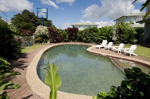 a swimming pool with white chairs next to a house at Barrier Reef Motel Innisfail in Innisfail