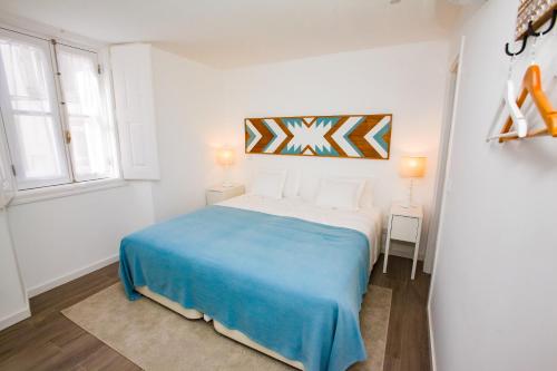 a white bedroom with a blue bed and two windows at Casas Madre de Deus in Évora