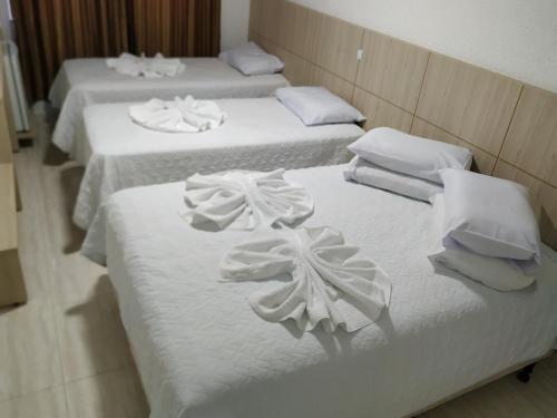 three beds in a room with white sheets and towels at Hotel Dove in Foz do Iguaçu