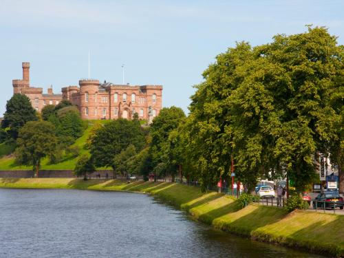 a castle with a river in front of a building at The Ness Guest House in Inverness