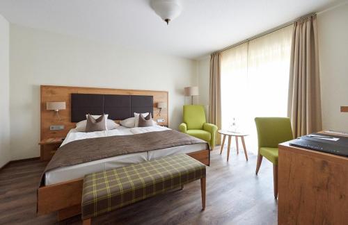 a bedroom with a bed and two green chairs at Fetzers Landhotel in Ingelheim am Rhein
