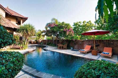 a swimming pool with two chairs and an umbrella at Pondok Mimpi Tulamben by AGATA in Tulamben