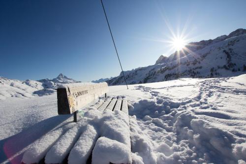 a bench in the snow with the sun in the background at Hotel Adler in Warth am Arlberg