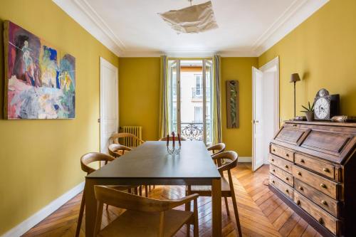 une salle à manger avec des murs jaunes et une table et des chaises en bois dans l'établissement Veeve - Muted Beauty in Batignolles, à Paris