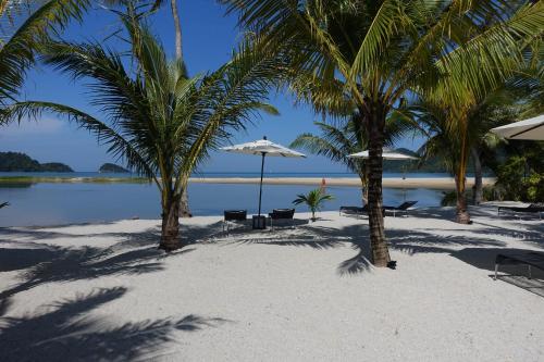 a beach with chairs and umbrellas and palm trees at Laguna Beach House in Ko Chang