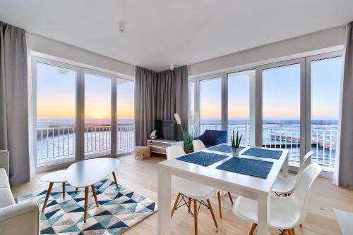 uma sala de estar com uma mesa e cadeiras brancas e janelas grandes em Apartamenty Marina z widokiem na morze em Darlowko