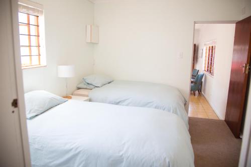 1 dormitorio con 2 camas blancas y ventana en Green Nook en Plettenberg Bay