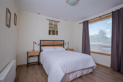 a white bedroom with a bed and a window at Huellas y Senderos Hotel in Coihaique