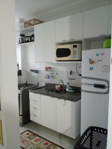 Una cocina con gabinetes blancos y un refrigerador blanco. en Prédio com piscina na cobertura frente ao mar, apartamento para até 6 pessoas e 3 crianças até 8 anos, churrasqueira na sacada, Wi-Fi grátis, NÃO oferecemos roupas de cama e banho, 1 vaga de garagem, na Praia Grande-Vila Mirim, en Praia Grande