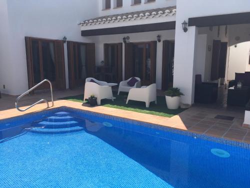 a swimming pool with white chairs and a house at Casa Catherina Joan - El Valle Golf Resort in Baños y Mendigo