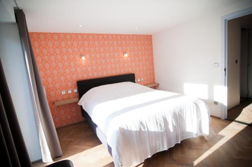 a bedroom with a white bed and an orange wall at Apartment De Maasnacht in Maaseik