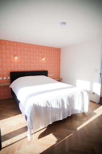a bedroom with a large white bed with an orange wall at Apartment De Maasnacht in Maaseik