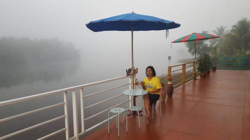 a woman sitting on a deck under an umbrella at Khum Thong Resort in Takua Pa