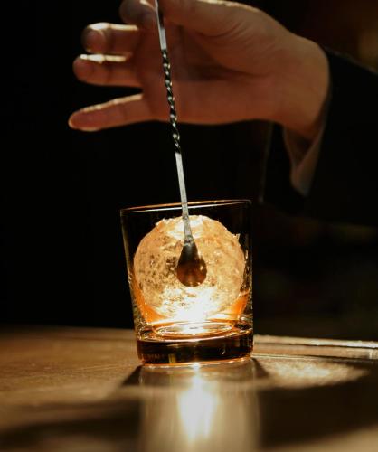 a hand holding a spoon in a glass of whiskey at Park Hotel Tokyo in Tokyo