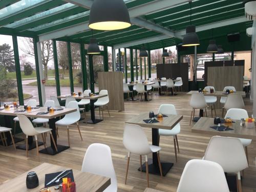 un restaurant avec des tables, des chaises et des fenêtres dans l'établissement Hôtel Motelia, à Moissy-Cramayel
