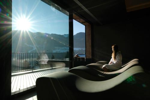 a woman sitting on a couch in front of a window at La Roccia Wellness Hotel in Cavalese