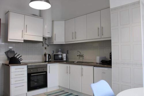 a white kitchen with white cabinets and a microwave at Margarida House - Stone Apartment in Ribeira Grande