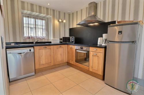 une cuisine avec des armoires en bois et un réfrigérateur en acier inoxydable dans l'établissement Gîte le Grand Bé, à Saint-Malo
