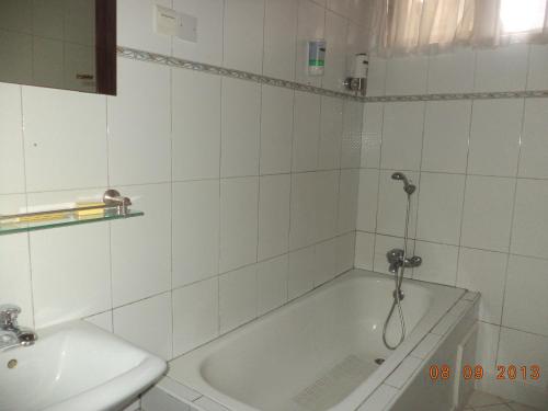 a white tiled bathroom with a tub and a sink at Royal Cockpit Hotels in Mpuase