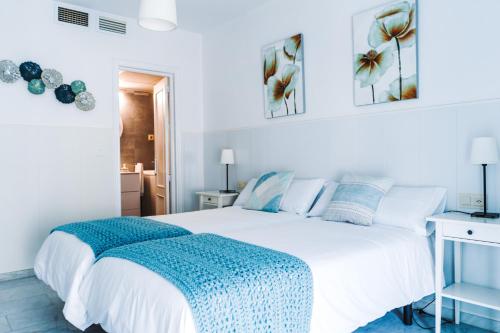 a bedroom with a white bed with a blue blanket on it at Apartamento Victoria con parking incluido in Ronda