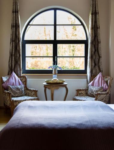 a bedroom with a bed and two chairs and a large window at Hofgut Holzmuhle in Germersheim