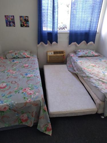 a bedroom with two beds and a window with blue curtains at Campo Grande Pousar ou morar in Rio de Janeiro