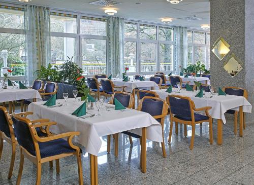 ein Esszimmer mit weißen Tischen, Stühlen und Fenstern in der Unterkunft Residenz & Hotel Am Kurpark in Schlangenbad