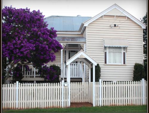 a white house with a white picket fence and a purple tree at Ashbrooke Cottage in Toowoomba