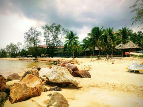 a beach with rocks and palm trees and a building at Bebe Homestay Phu Quoc in Phu Quoc