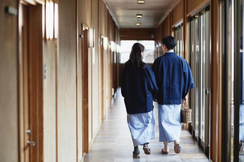 a man and a woman walking down a hallway at Takamiya Ryokan Sagiya Sansorai in Kaminoyama
