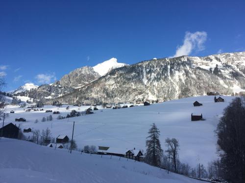 a snow covered hill with houses and mountains at Ferienwohnung Haus am Bach in Toggenburg in Wildhaus