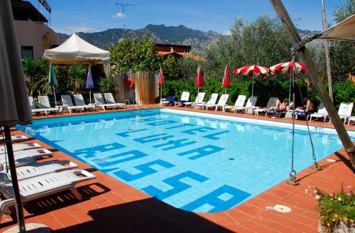 una gran piscina con sillas y sombrillas en Ambienthotel Luna Rossa en Malcesine
