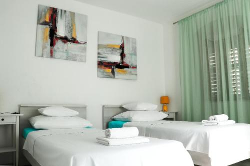 two beds in a white room with paintings on the wall at Apartman Ana in Skradin