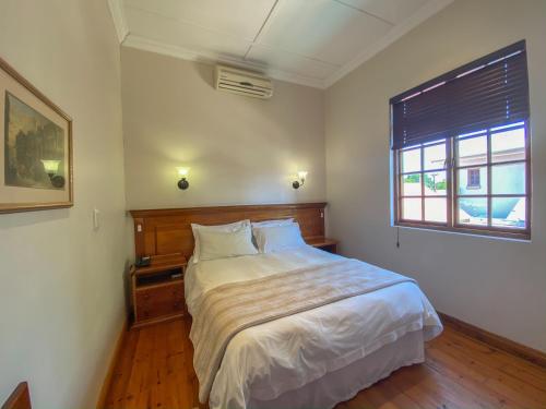 Schlafzimmer mit einem Bett mit weißer Bettwäsche und einem Fenster in der Unterkunft Turnberry Boutique Hotel in Oudtshoorn