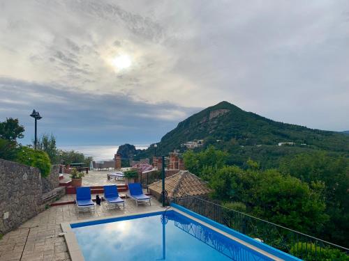 a swimming pool with two blue chairs and a mountain at Ermones Emerald Villa in Vátos