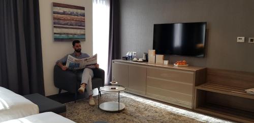 a man sitting in a chair reading a newspaper in a hotel room at Swiss-Belboutique Bneid Al Gar Kuwait in Kuwait