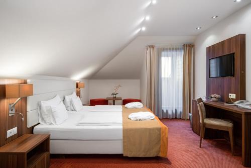 a hotel room with a large white bed and a desk at Bükkös Hotel & Spa in Szentendre