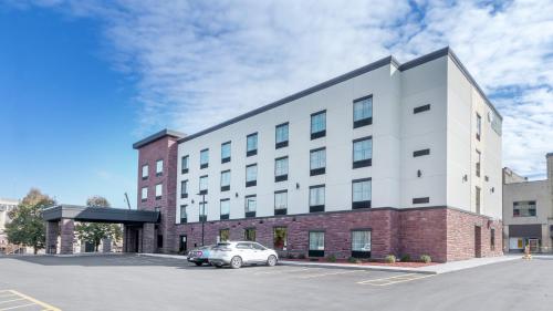 a building with a car parked in a parking lot at Cobblestone Hotel & Suites - Janesville in Janesville