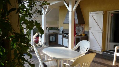 une table et des chaises blanches sur une terrasse couverte avec une cuisine dans l'établissement Au Bras d'Argent, à Berthez