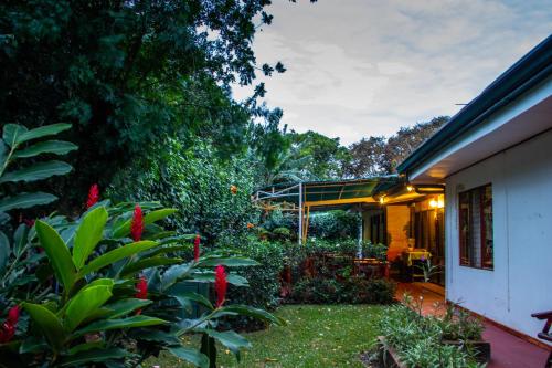 a garden with red flowers and a house at Hotel La Rosa de America in Alajuela City
