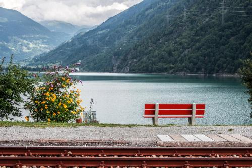a red bench sitting in front of a lake at Hotel Bed & Rooms , Corte Rossa -1 Min Walk To Bernina Express in Tirano