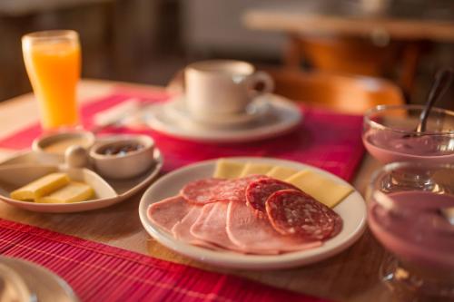 a table with a plate of ham and cheese and orange juice at Pousada Colina Verde in Garopaba