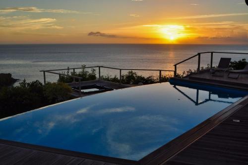 a swimming pool with a sunset over the ocean at Infiniti Blue in Bouillante