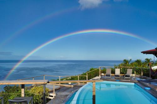 a rainbow over a swimming pool with a view of the ocean at Infiniti Blue in Bouillante