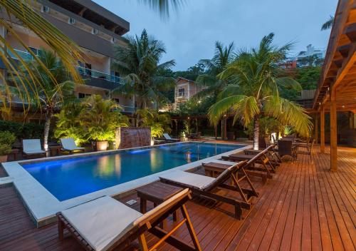 a swimming pool with chaise lounges and chairs next to a building at Pousada Castellammare in Bombinhas