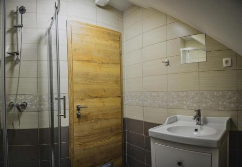 ein Badezimmer mit einem Waschbecken und einer Dusche mit einer Holztür in der Unterkunft Ta Fabrika Restavracija,pizzerija in prenočišča in Dravograd