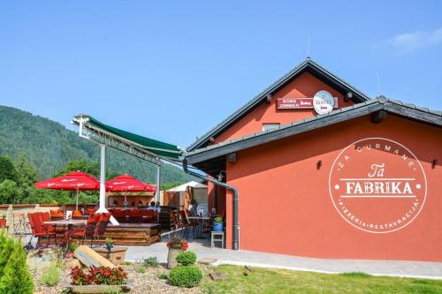 un edificio rojo con un restaurante con mesas y sombrillas en Ta Fabrika Restavracija,pizzerija in prenočišča, en Dravograd