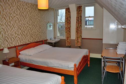 ロンドンにあるロンド ンビジターズ ホテルのベッド2台、テーブル、シンクが備わるホテルルームです。