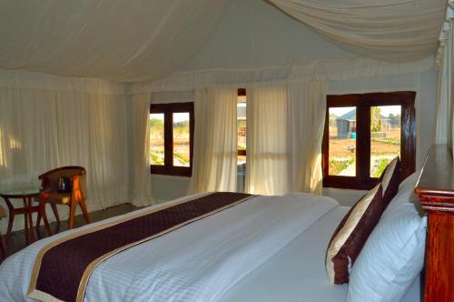 um quarto com uma grande cama branca e janelas em Thour Nature Resort - Jawai Leopard Safari Camp em Bera